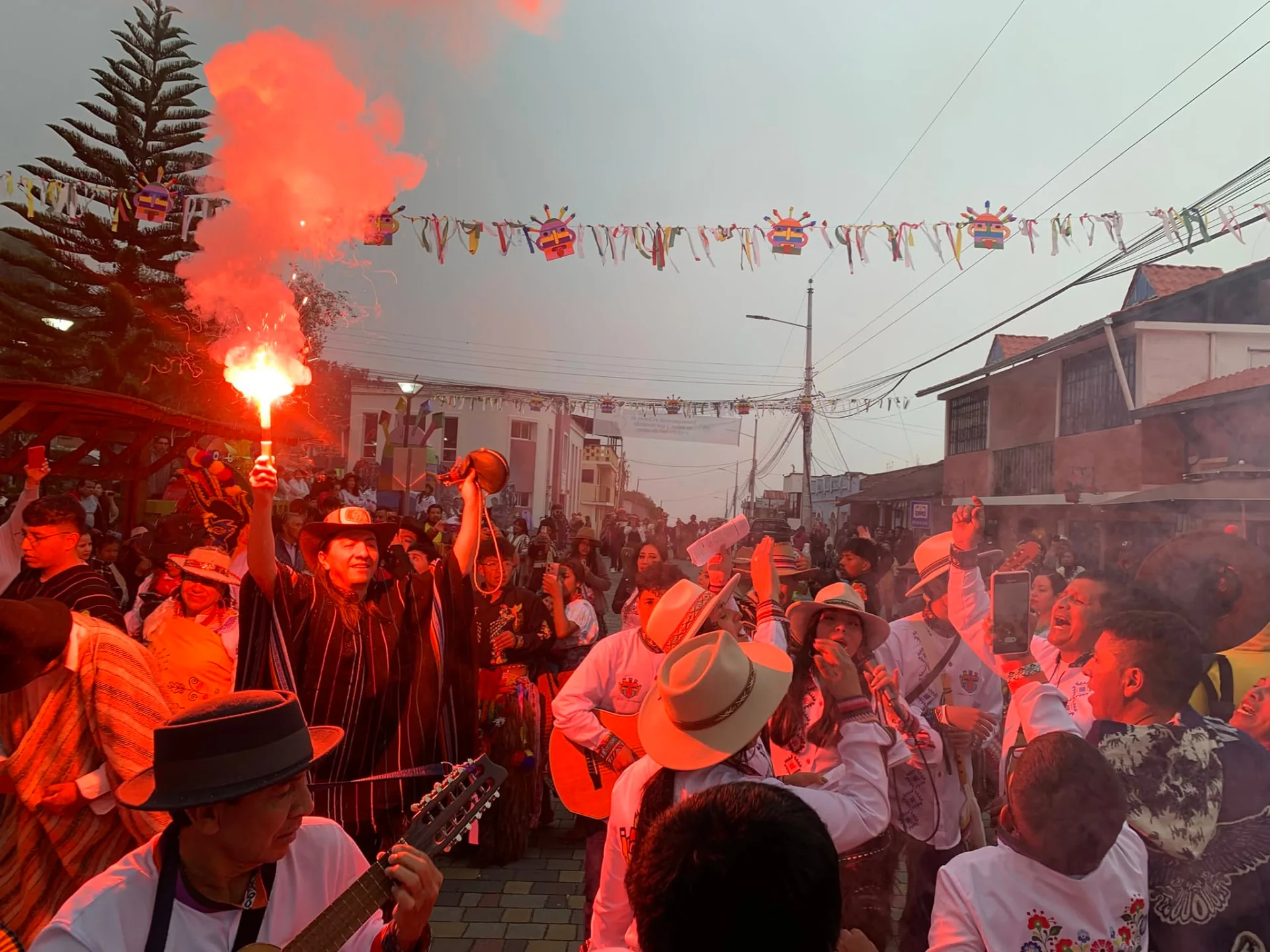 Músicos y vecinos celebran en una calle de Chavezpamba, iluminados por el resplandor rojo de una bengala.